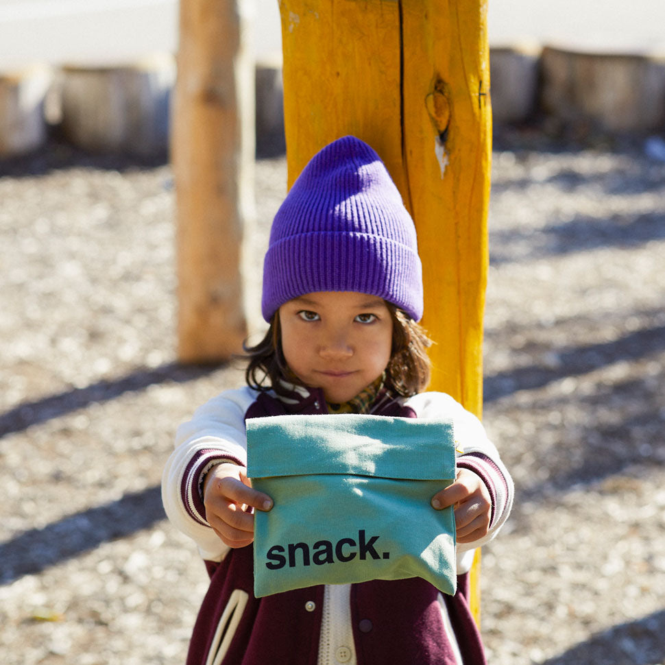 a kid holding Reusable and machine washable blue and white polka dots snack bag in a sandwich size. Part of the Fluf Lunch collection 