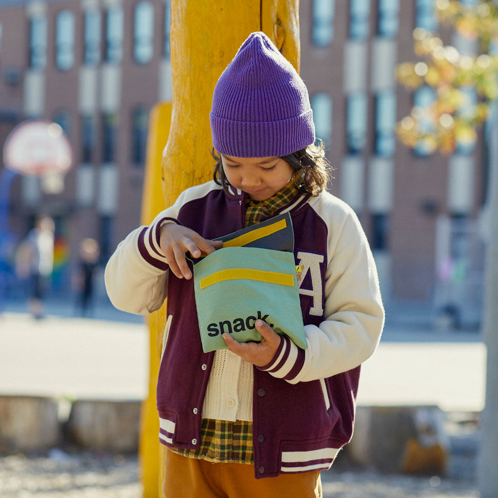 a kid open Reusable and machine washable blue and white polka dots snack bag in a sandwich size. Part of the Fluf Lunch collection 