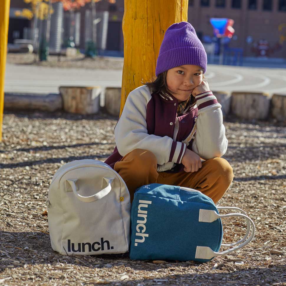 Unisex lunch bag in natural color and 'lunch' motif and a kid sitting by.